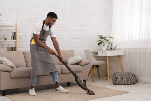 African-american man cleaning house with wireless vacuum cleaner, making housework alone, copy space